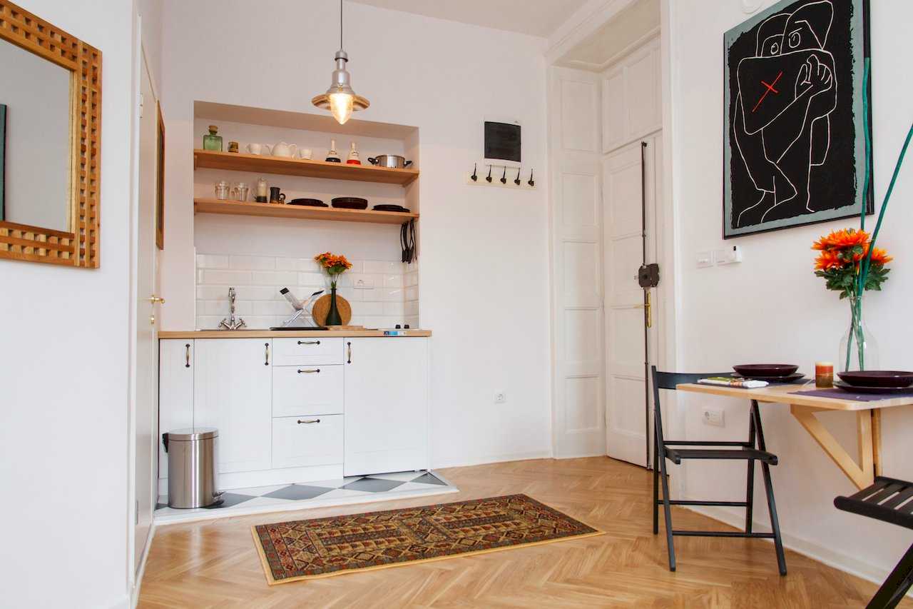 Kuhinja u niši sa belim elementima i otvorenim policama, sto za dvoje uz zid – Apartman Atelje 1 – City Break Apartments