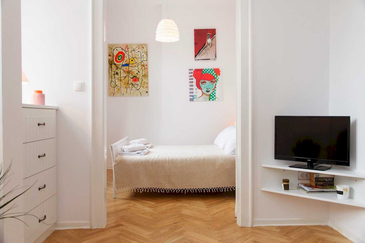 Pogled ka spavaćoj sobi sa bračnim krevetom i zidnim TV-om na polici – Apartman Atelje 1 – City Break Apartments