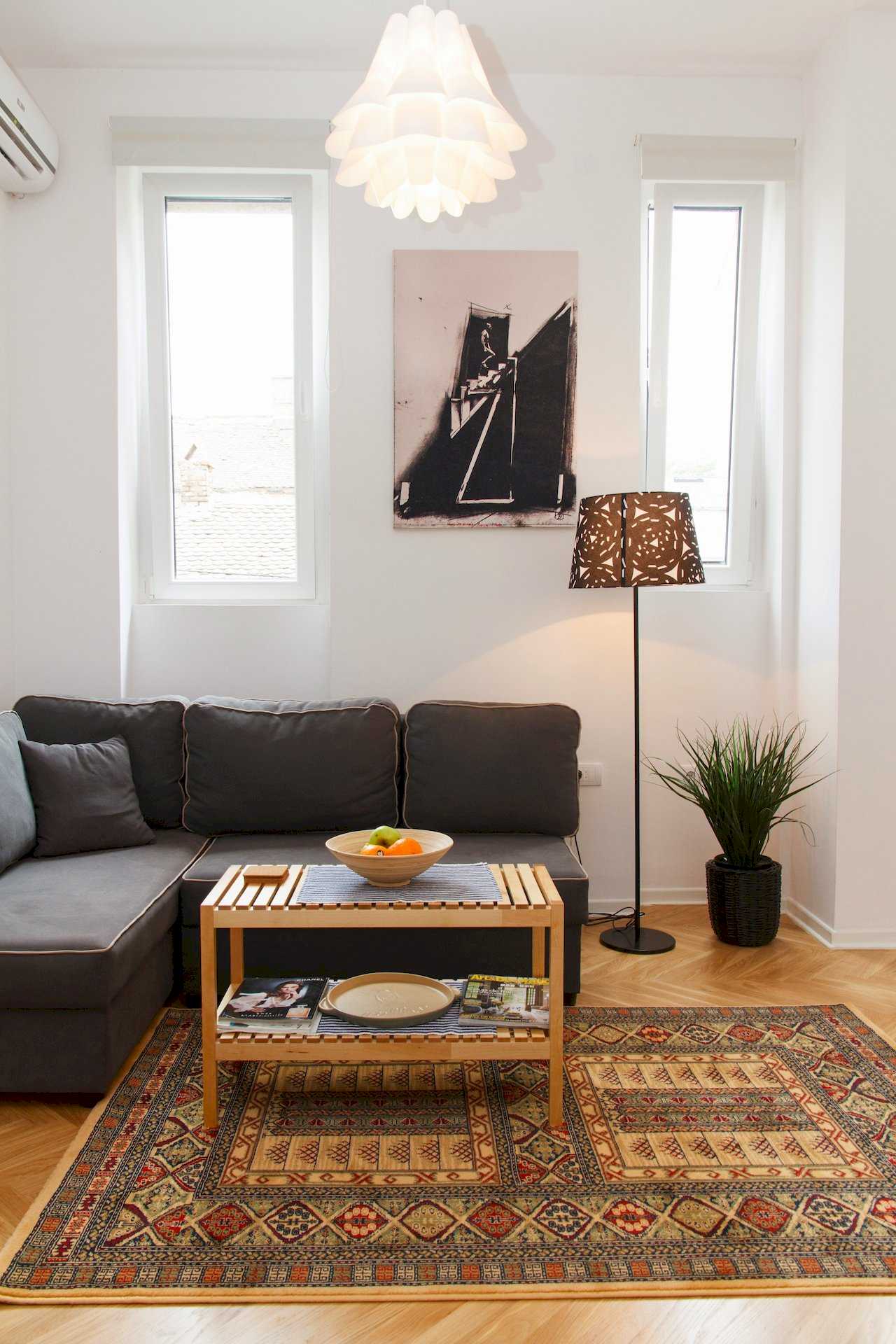 Ugaona garnitura, klub sto i podna lampa pored prozora – Apartman Atelje 1 – City Break Apartments
