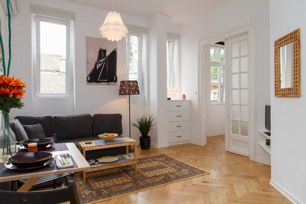 Dnevni boravak sa trpezarijskim stolom, ćilimom i staklenim vratima ka spavaćoj – Apartman Atelje 1 – City Break Apartments