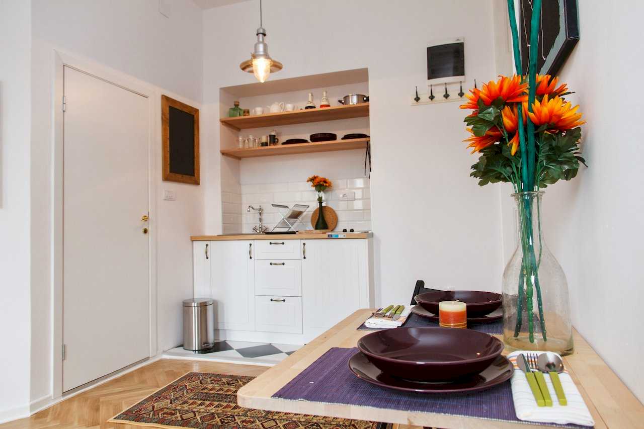 Trpezarijski sto u prvom planu i kuhinja u niši u pozadini – Apartman Atelje 1 – City Break Apartments