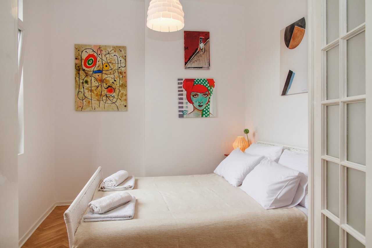 Spavaća soba sa bračnim krevetom, peškirima i umetničkim slikama na zidu – Apartman Atelje 1 – City Break Apartments