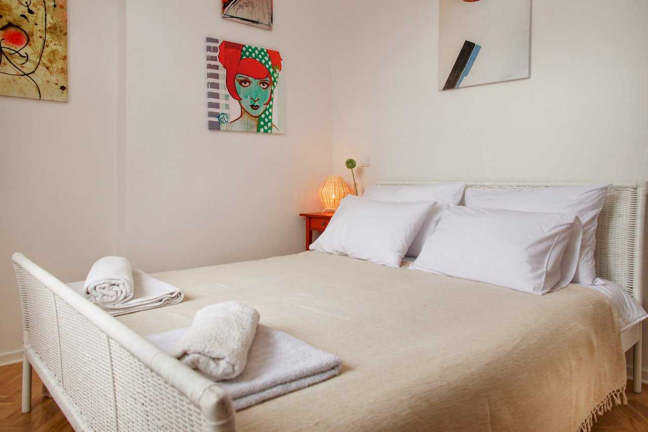 Detalj bračnog kreveta sa jastucima i noćnom lampom na crvenom stočiću – Apartman Atelje 1 – City Break Apartments