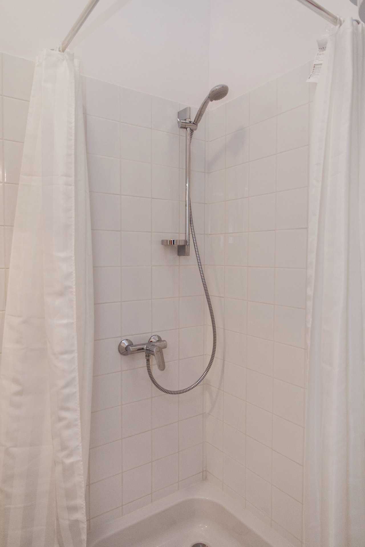 Tuš kabina sa belim pločicama i ručnim tušem – Apartman Atelje 1 – City Break Apartments