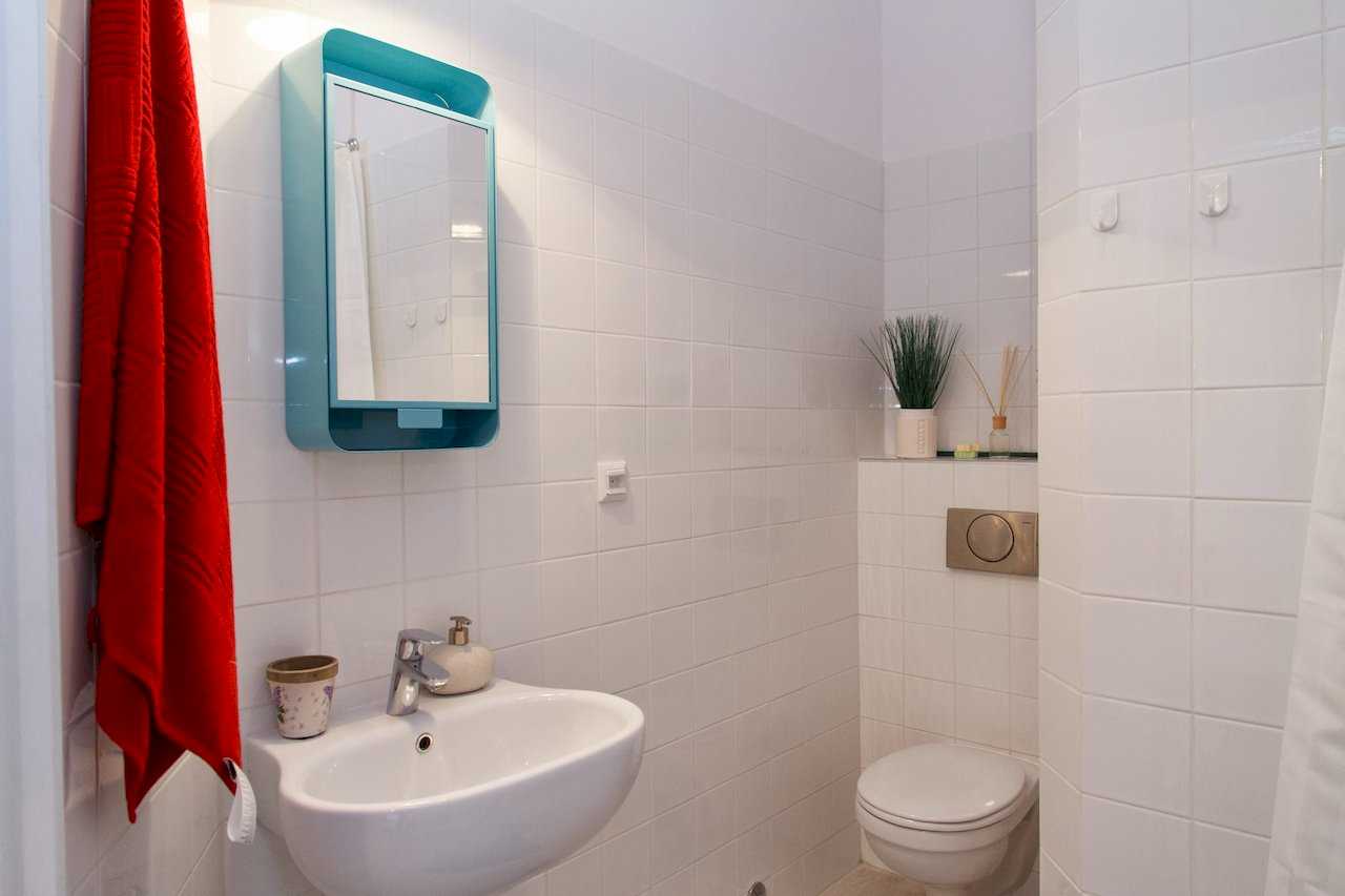 Kupatilo sa lavaboom, ogledalom u tirkiznom ramu i crvenim peškirom – Apartman Atelje 1 – City Break Apartments