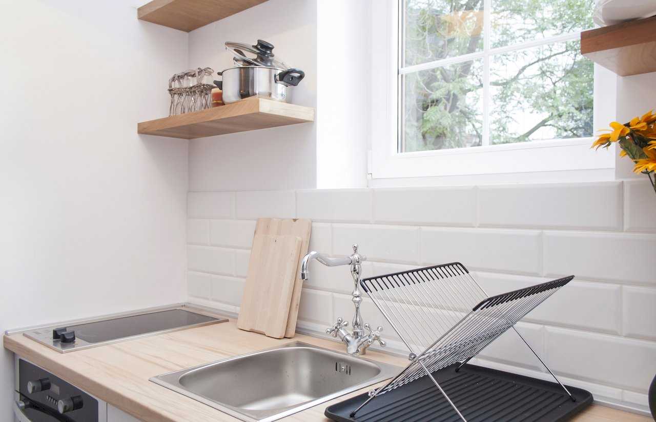 Kitchen detail – stainless sink with classic chrome tap, two-zone induction hob, wooden cutting boards leaning against the wall, wire dish rack and open wooden shelves with a stainless pot – Apartment Atelje 2 – City Break Apartments