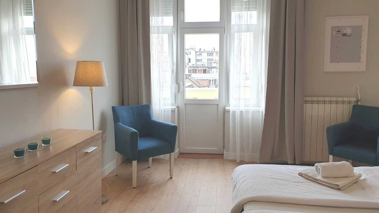 Bedroom with dresser, floor lamp and armchair by the balcony door – Apartment Cityzen – City Break Apartments