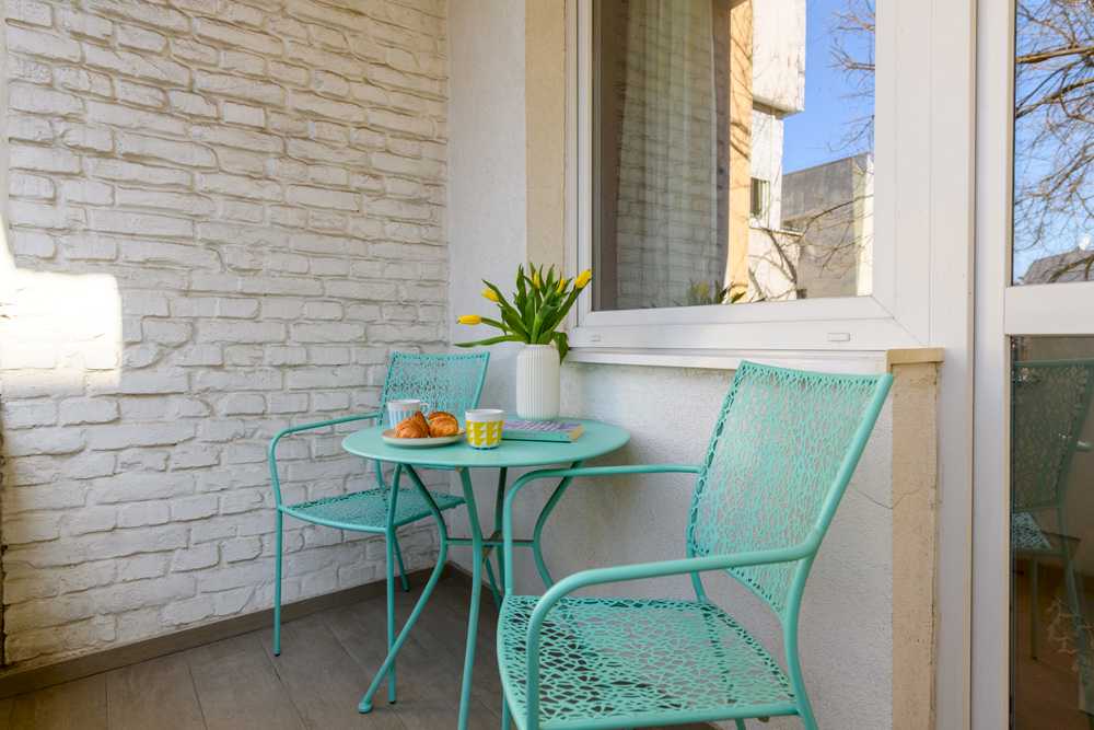 Mala terasa sa zidom od bele cigle, mint okruglim stolom i dve mint metalne lace stolice, vazom sa žutim tulipanima i jutarnjim posluženjem – Apartman Design – City Break Apartments