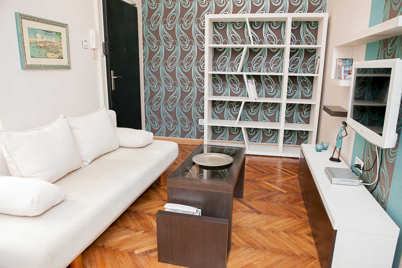 Apartment Downtown (Skadarlija, Belgrade) – living room with white sofa, bookcase and TV unit