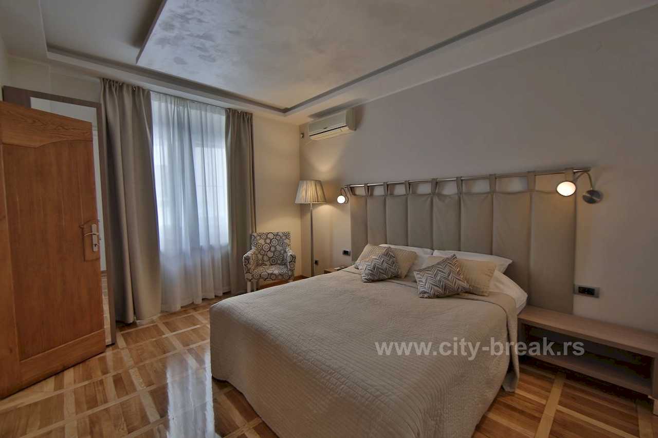 Bedroom with a double bed, padded headboard and curtained window – Apartment Jovanova Lux – City Break Apartments