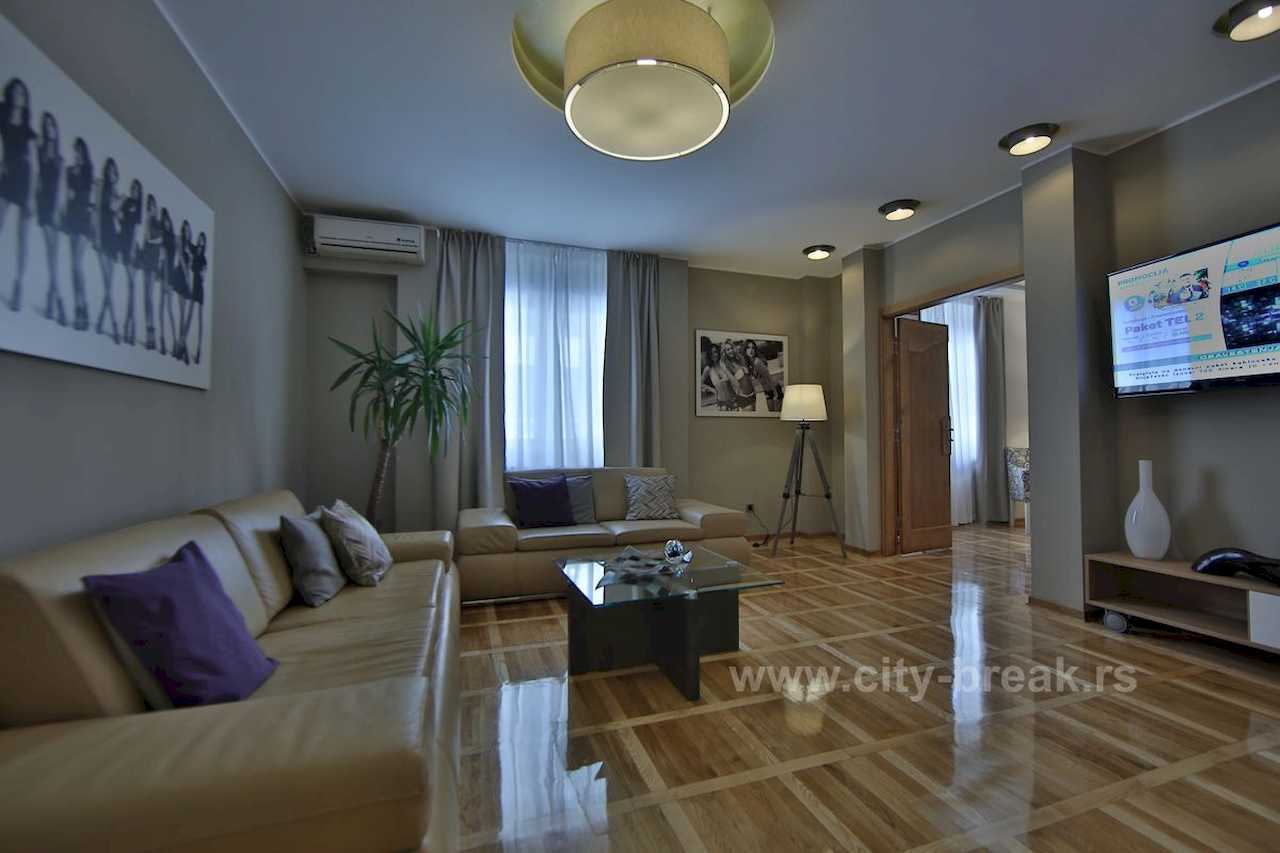 Living room with sofas, wall-mounted TV, glass coffee table and tripod floor lamp – Apartment Jovanova Lux – City Break Apartments