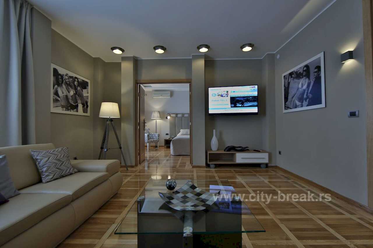 Living room with a glass coffee table and view into the bedroom with a double bed – Apartment Jovanova Lux – City Break Apartments