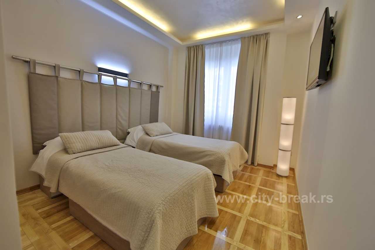 Bedroom with two single beds, wide padded headboard and wall-mounted TV – Apartment Jovanova Lux – City Break Apartments