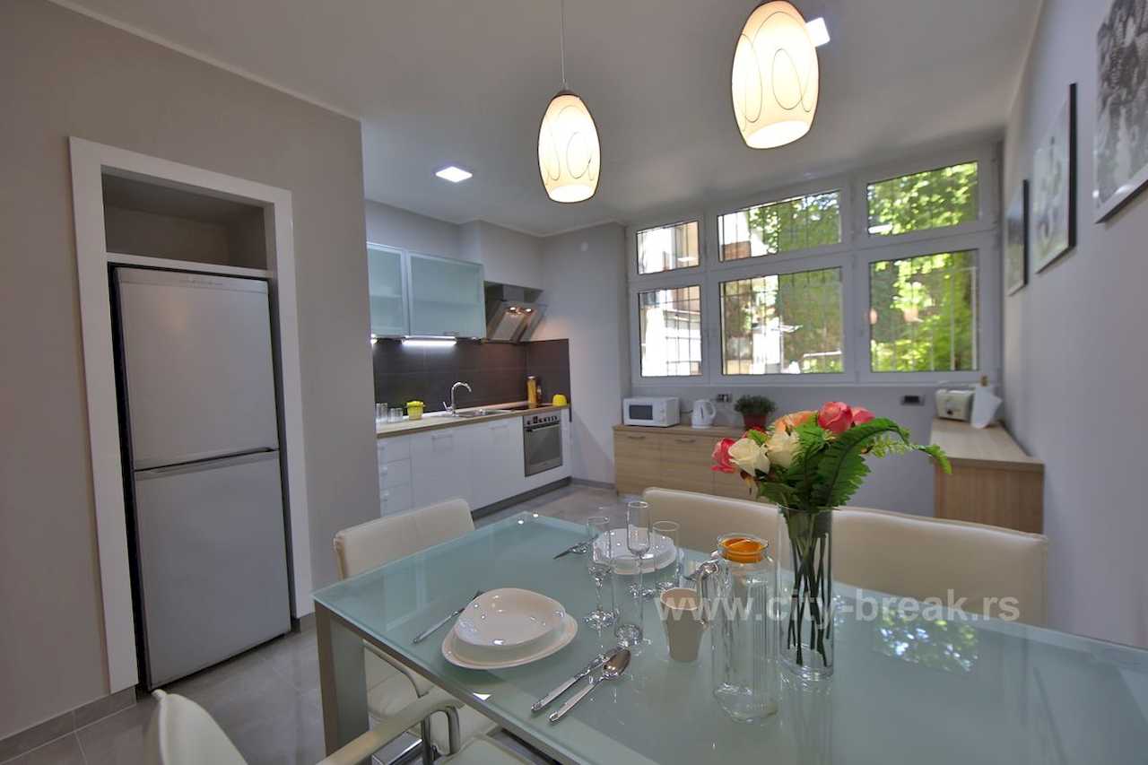 Kitchen and dining area with a glass table, flowers and white cabinetry – Apartment Jovanova Lux – City Break Apartments