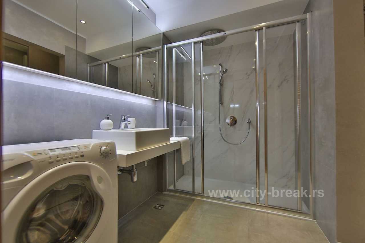 Bathroom with LED-backlit mirror, shower enclosure and washing machine – Apartment Jovanova Lux – City Break Apartments