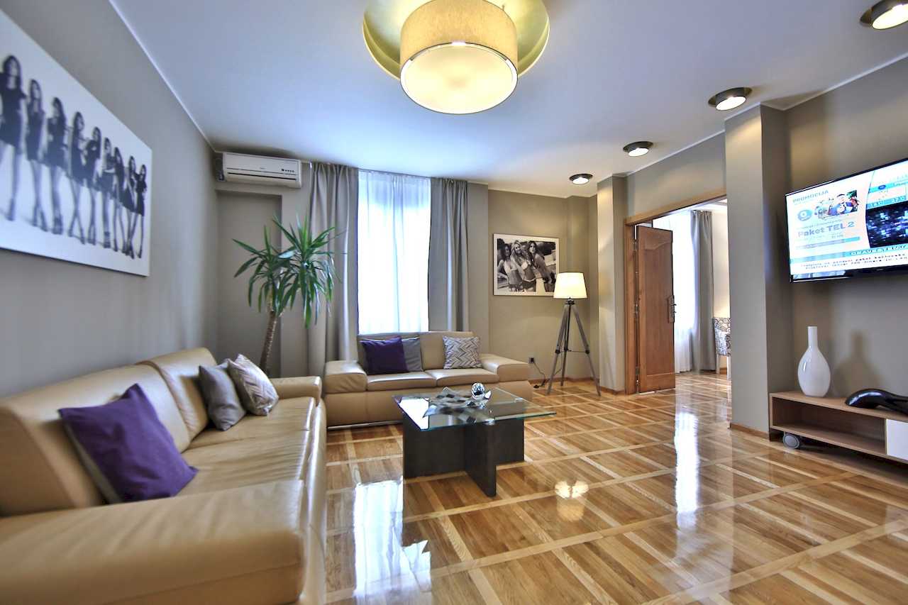 Living room with leather sofas, wall-mounted TV and a tall plant in the corner – Apartment Jovanova Lux – City Break Apartments