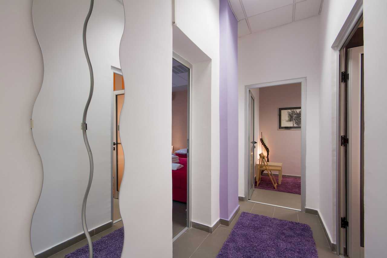 Hallway with wavy wall mirror, purple rugs, and views into bedrooms – Apartment Klio – City Break Apartments