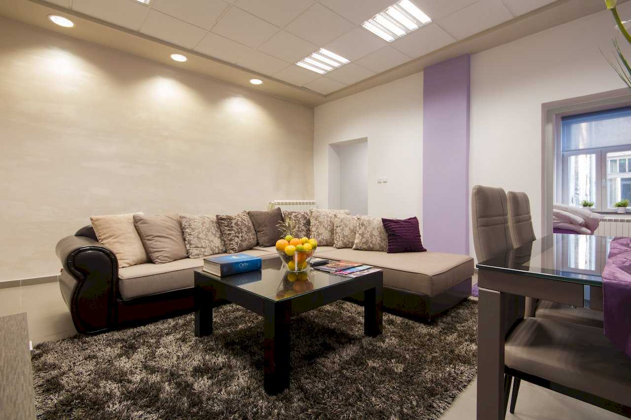 Sectional with brown leather trim and cushions, square coffee table, and dining corner with purple runner – Apartment Klio – City Break Apartments