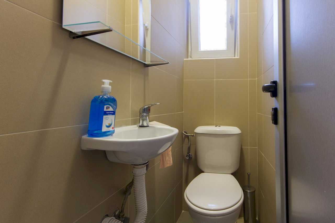 Compact guest toilet with wall-mounted sink, mirrored cabinet, toilet, bidet shower, brush holder, and small window – Apartment Klio – City Break Apartments