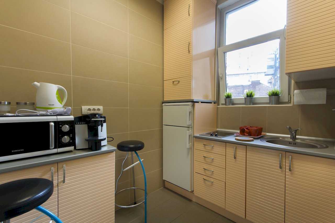 Compact kitchen with ribbed wood cabinets, grey countertops, microwave, espresso machine, kettle, and bar stools – Apartment Klio – City Break Apartments