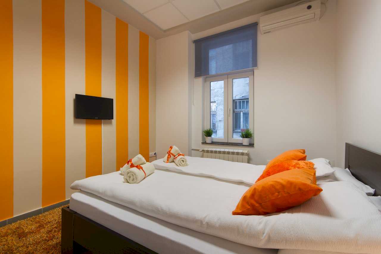Bedroom with double bed, orange-and-white striped wall, wall TV, orange pillows, and shag rug – Apartment Klio – City Break Apartments