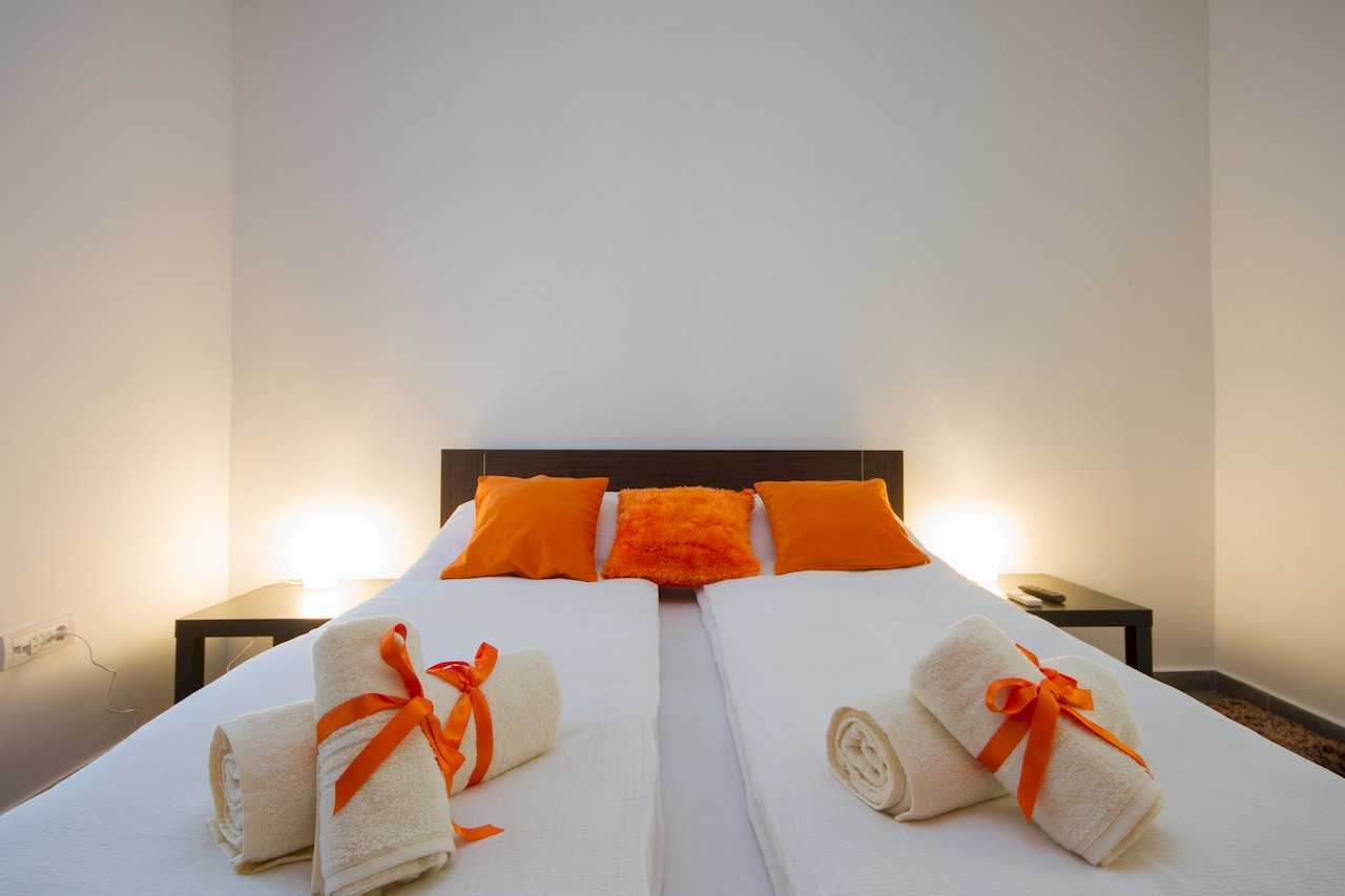 Bedroom with double bed, orange pillows, and lit lamps on dark wood nightstands – Apartment Klio – City Break Apartments