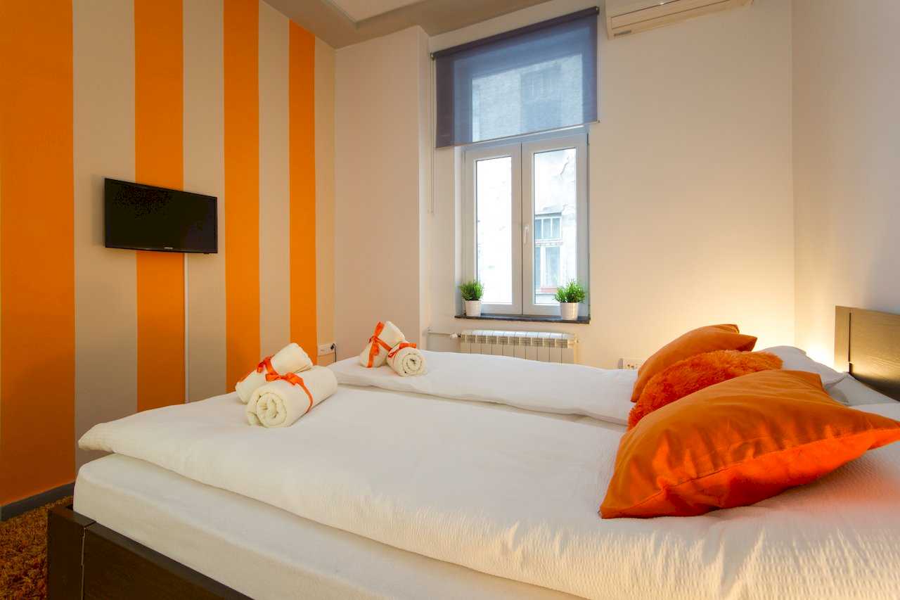 Bedroom with orange-and-white vertical stripes, double bed, and TV mounted above the bed – Apartment Klio – City Break Apartments