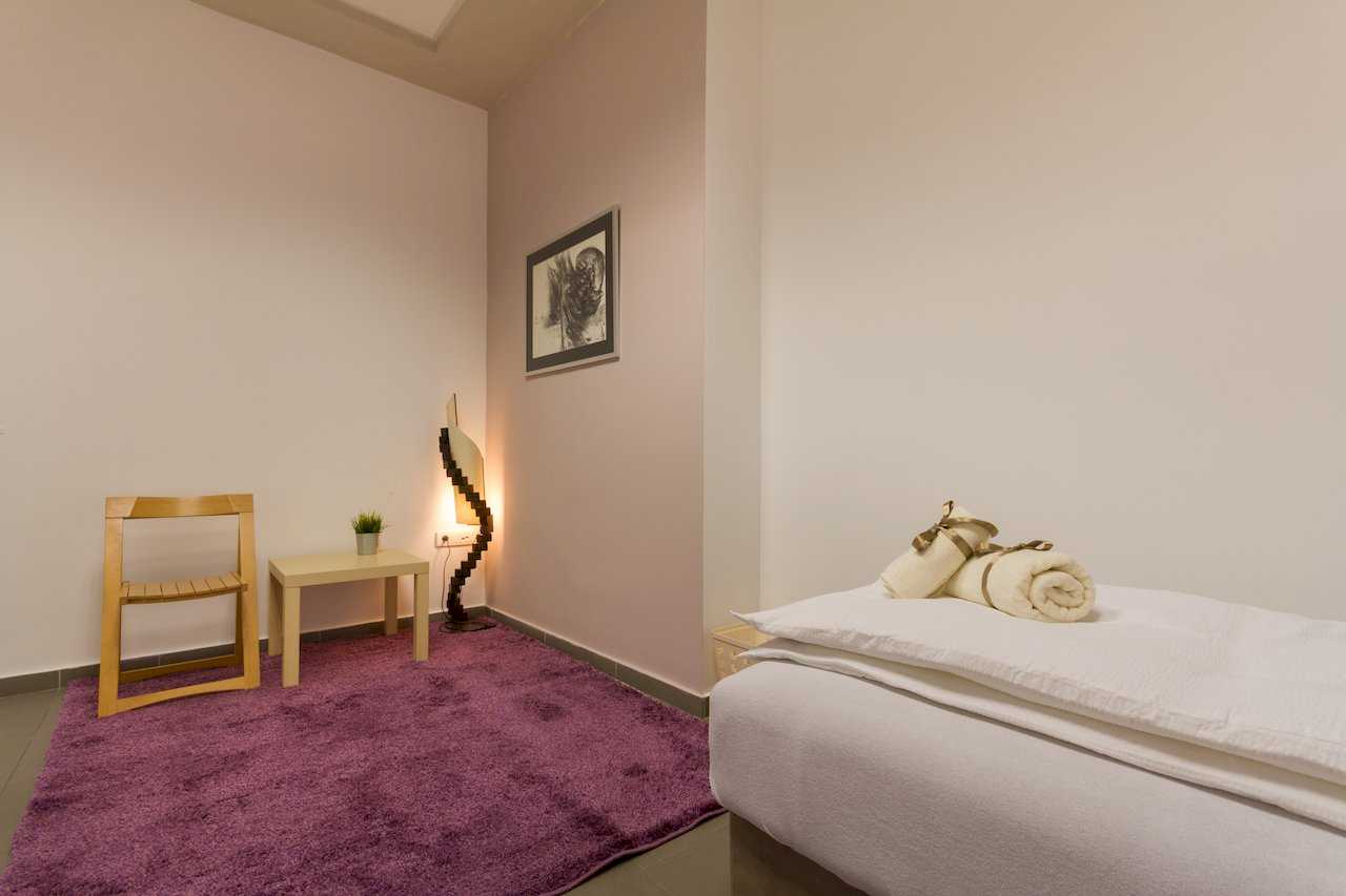 Corner with purple shag rug, wooden chair and side table, sculptural floor lamp, and bed in foreground – Apartment Klio – City Break Apartments