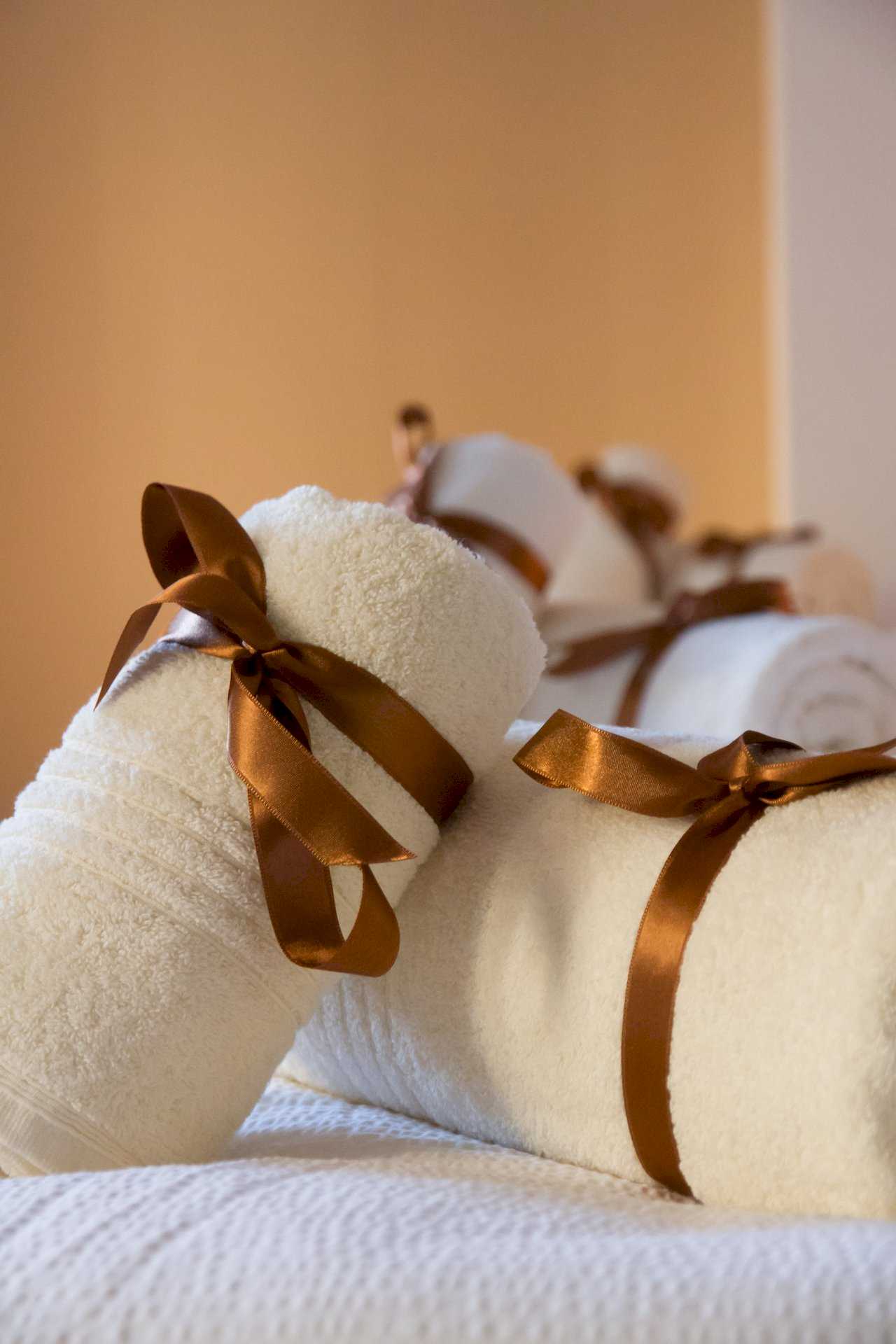 Close-up of rolled white towels with brown satin bows on the bed – Apartment Klio – City Break Apartments