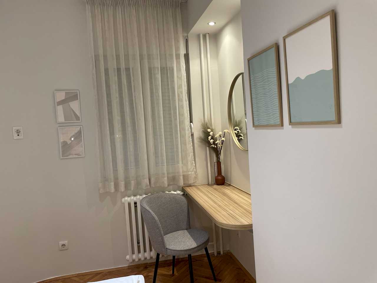 Work corner with floating wood desk, grey upholstered chair, round gold-framed mirror and abstract wall art – Klishe Zen Apartment – City Break Apartments