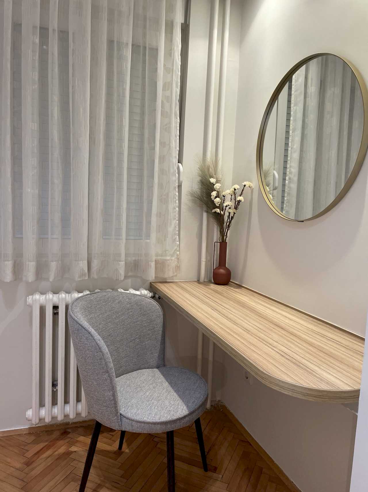 Close-up of floating wood desk, grey chair, round gold-framed mirror and vase with dried flowers – Klishe Zen Apartment – City Break Apartments