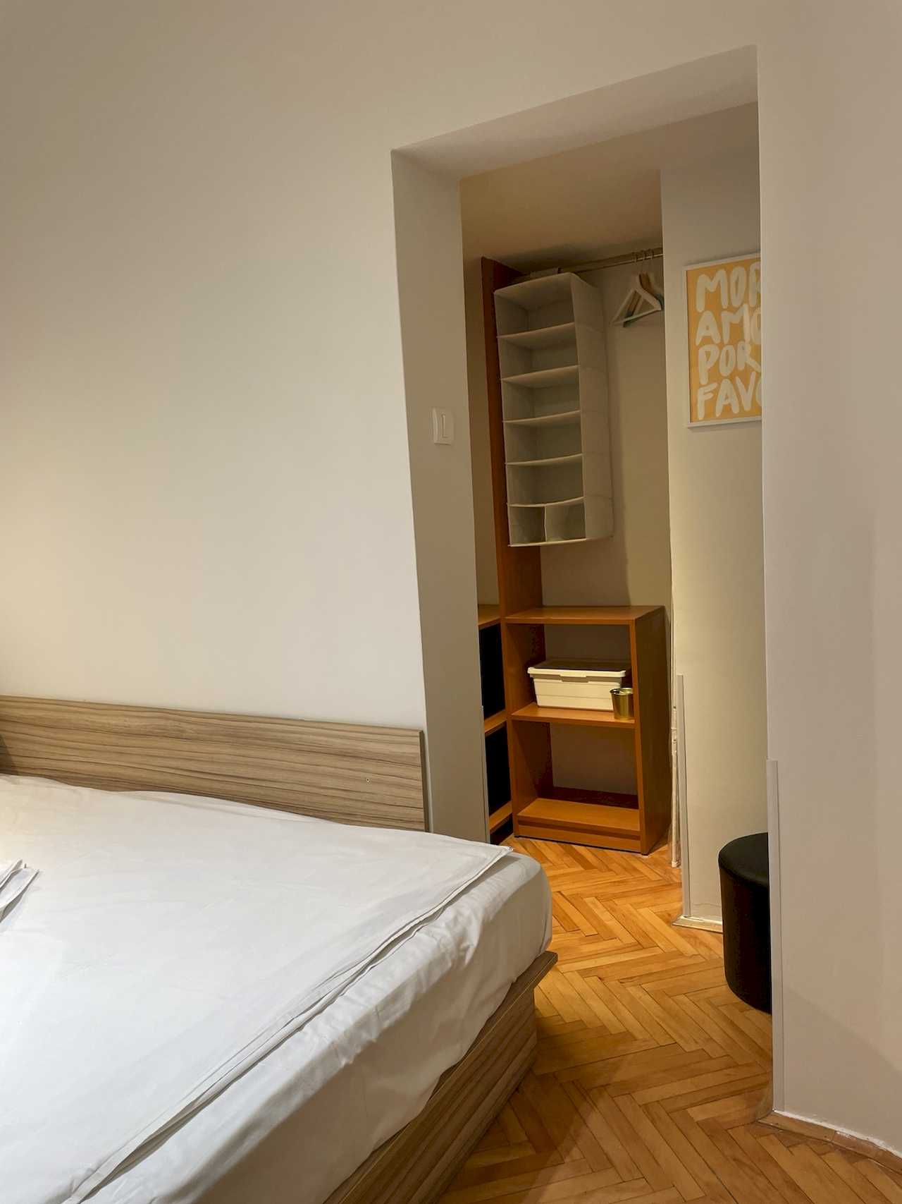 Bedroom with bed and built-in walk-in closet – wood shelves, hangers, fabric organizer and yellow poster on the wall – Klishe Zen Apartment – City Break Apartments