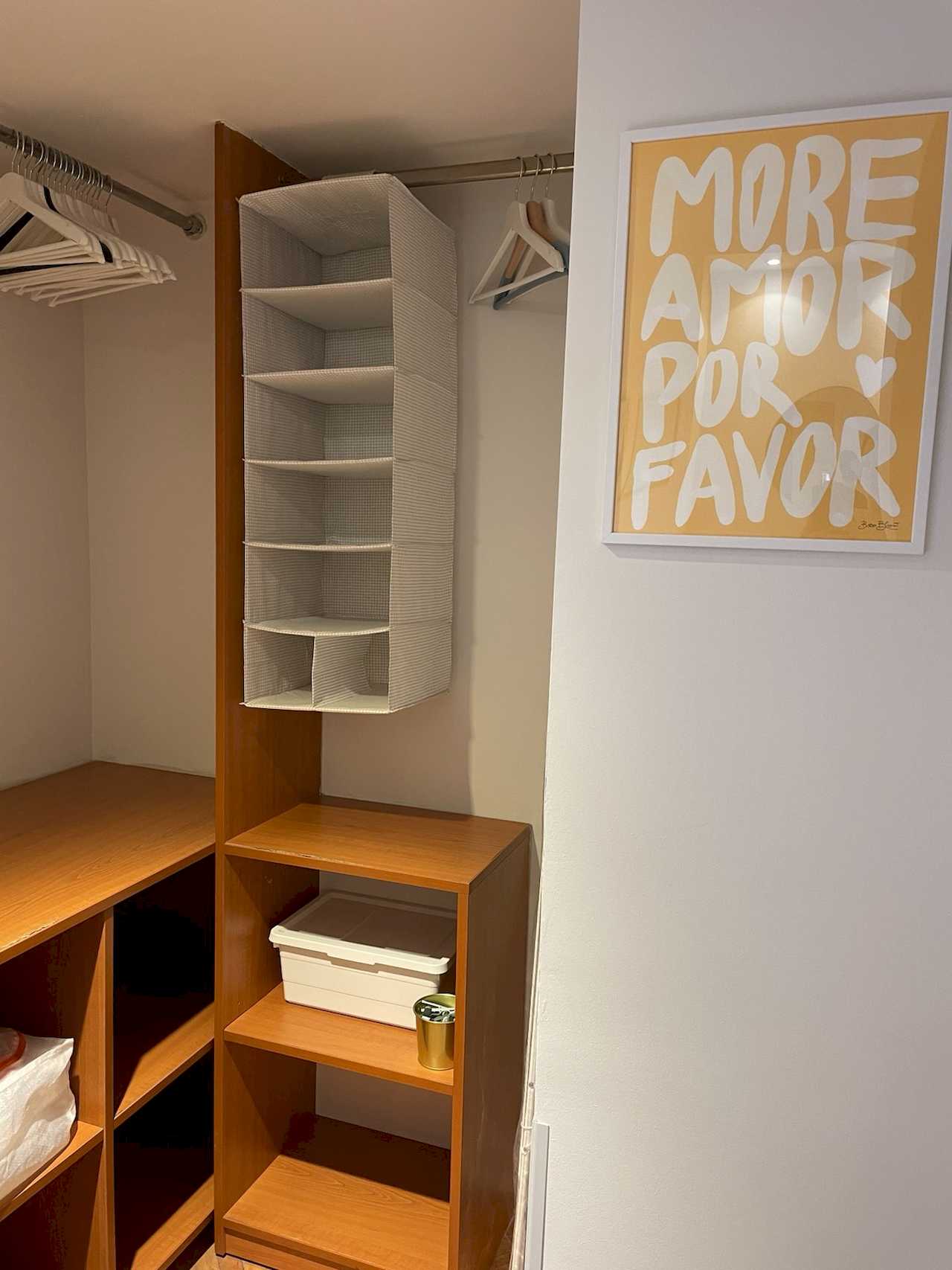 Walk-in closet with wood shelves, hanging organizer, hangers and yellow poster on the wall – Klishe Zen Apartment – City Break Apartments