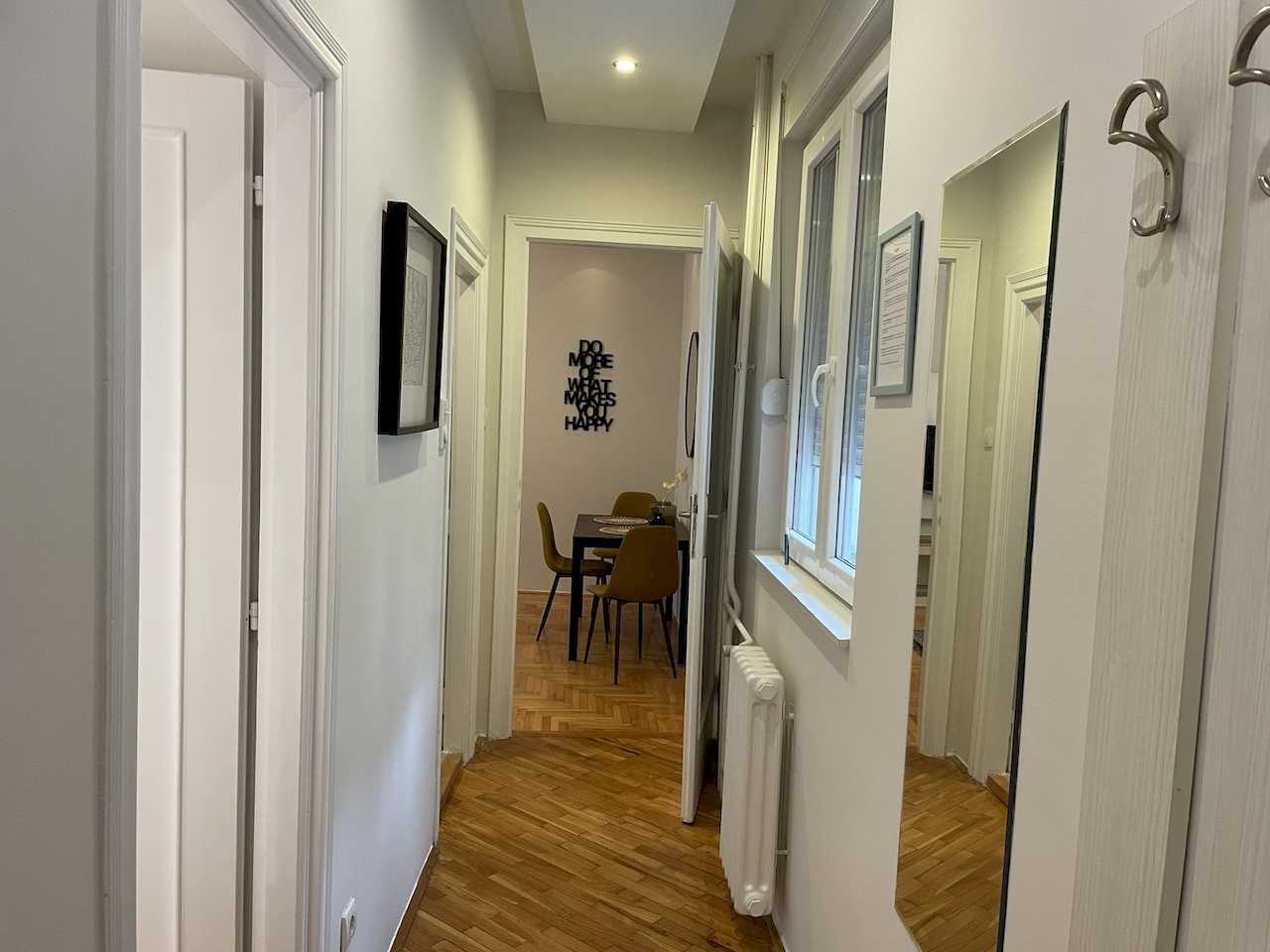 Hallway with tall wall mirror, radiator under a window and view toward the dining area with wall quote – Klishe Zen Apartment – City Break Apartments