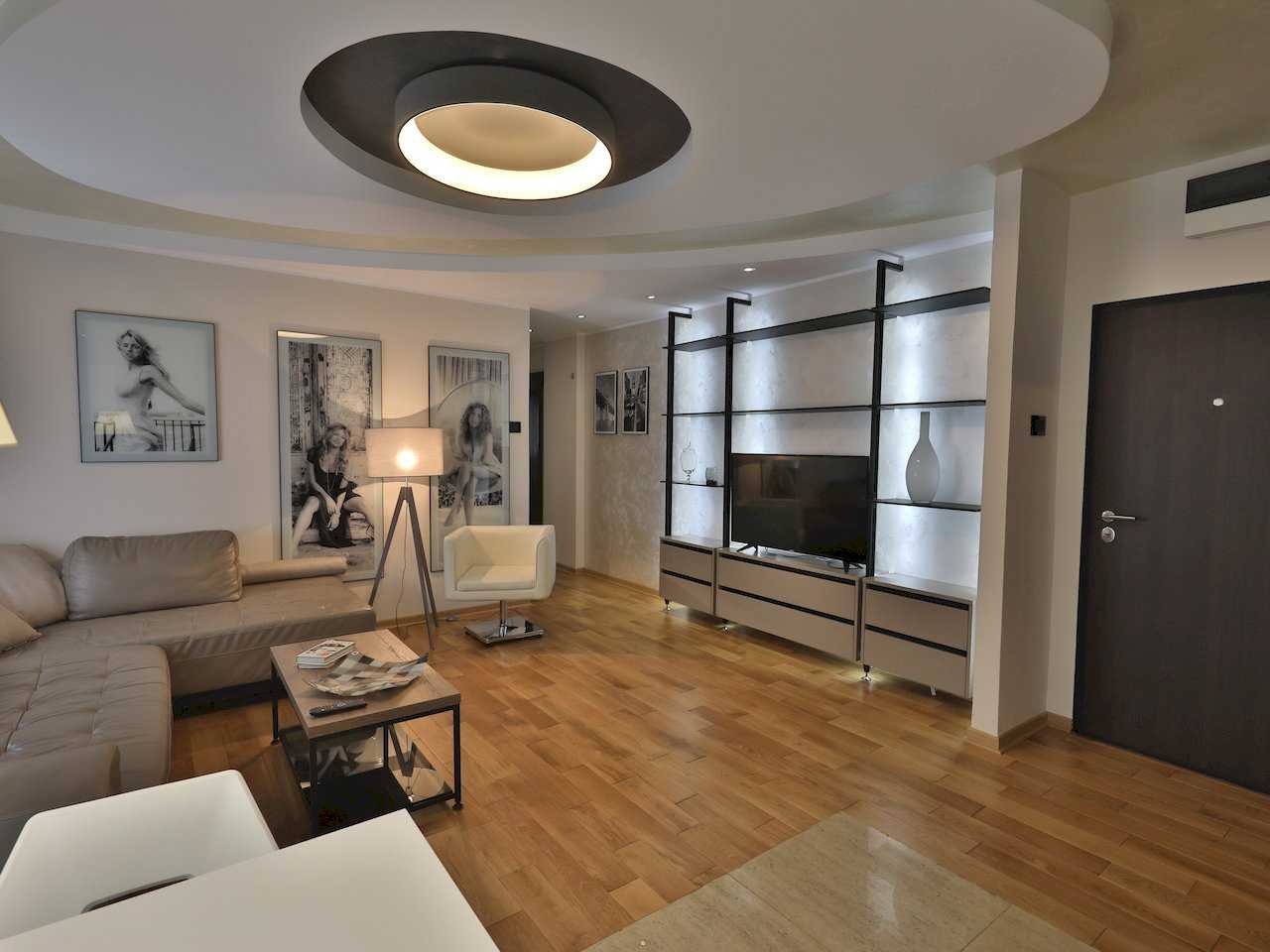 Dnevna soba sa kožnom ugaonom garniturom, TV zidom i kružnim plafonskim osvetljenjem – Apartman Luna Lux – City Break Apartments