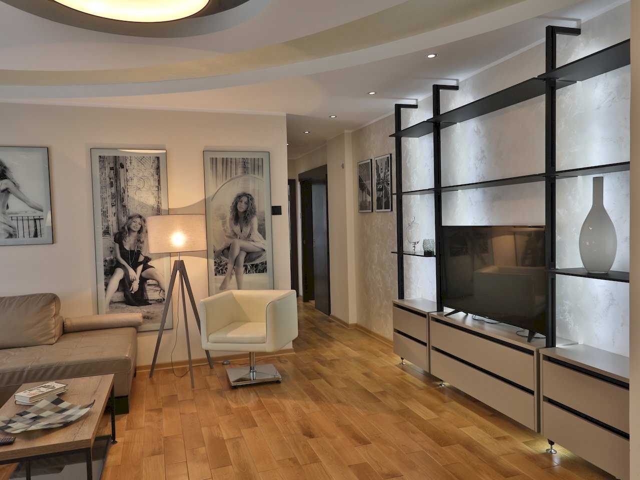 Dnevna soba sa kožnom sofom, belom foteljom i velikom policom za TV – Apartman Luna Lux – City Break Apartments