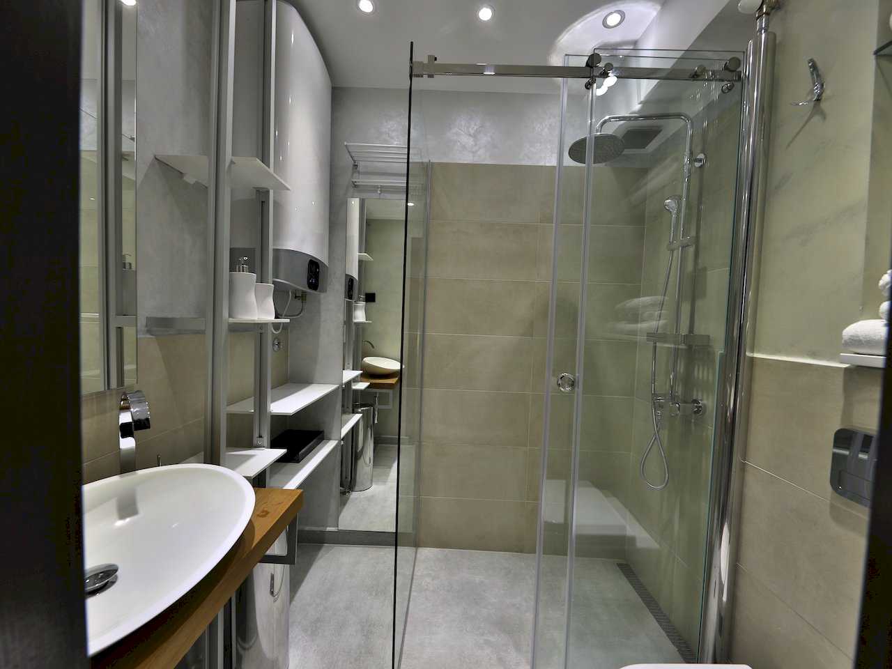 Kupatilo sa ovalnim lavaboom, policama, staklenom tuš kabinom i bojlerom – Apartman Luna Lux – City Break Apartments