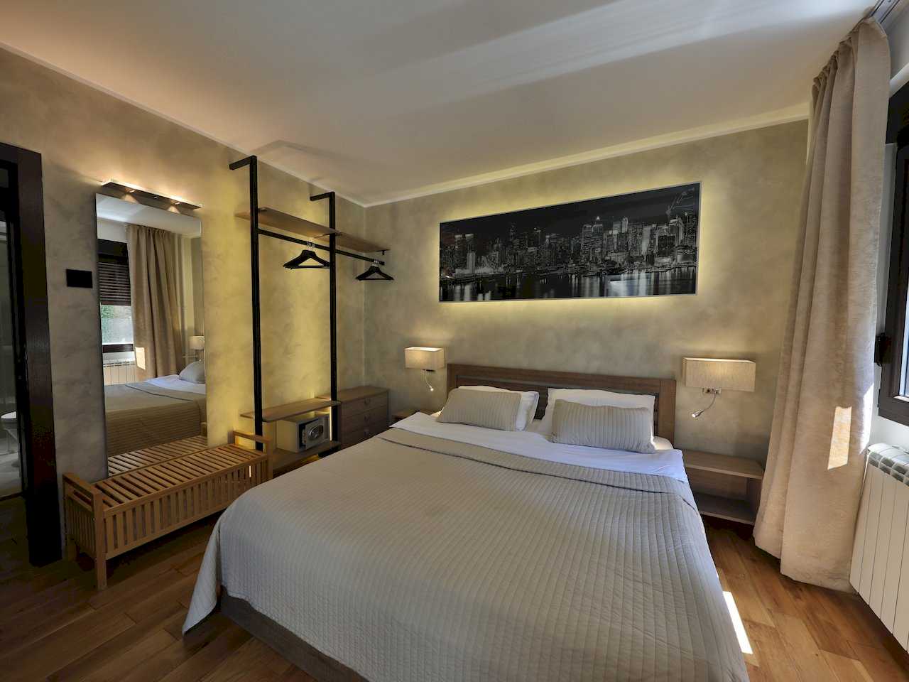 Spavaća soba sa bračnim krevetom, otvorenim garderoberom i osvetljenom slikom grada – Apartman Luna Lux – City Break Apartments
