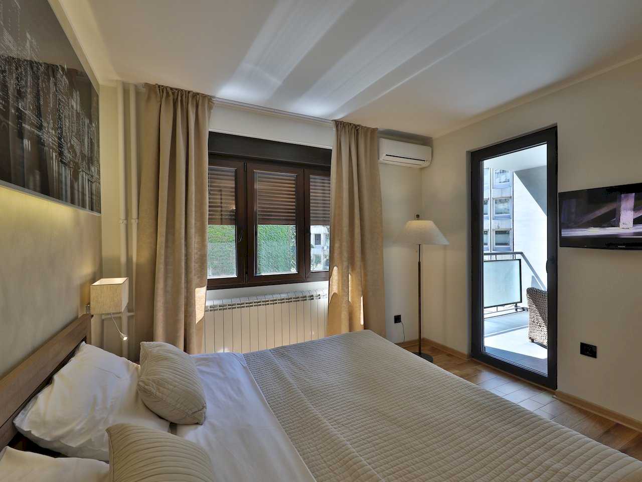 Spavaća soba sa bračnim krevetom, prozorom i staklenim vratima na terasu – Apartman Luna Lux – City Break Apartments