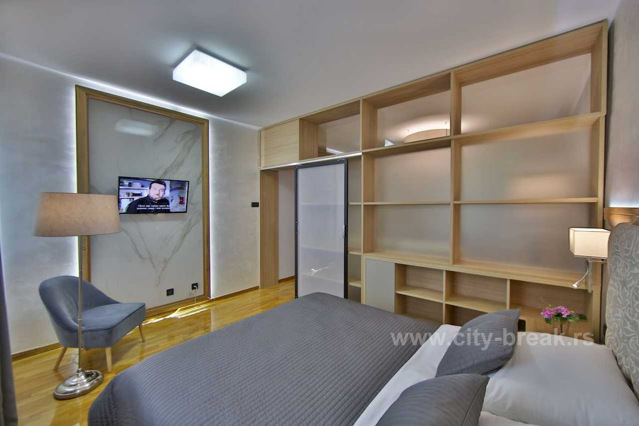 Spavaća soba sa bračnim krevetom, mermernim TV panelom sa pozadinskim svetlom i velikom drvenom policom-pregradom – Apartman Merkator – City Break Apartments