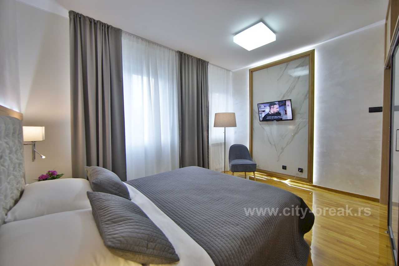 Spavaća soba sa bračnim krevetom, LED osvetljenjem iza TV panela i delom plakara sa ogledalom – Apartman Merkator – City Break Apartments
