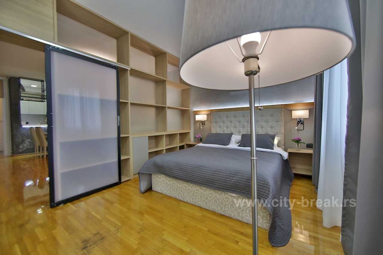 Spavaća soba sa bračnim krevetom, ugradnom drvenom policom i kliznim staklenim vratima – Apartman Merkator – City Break Apartments