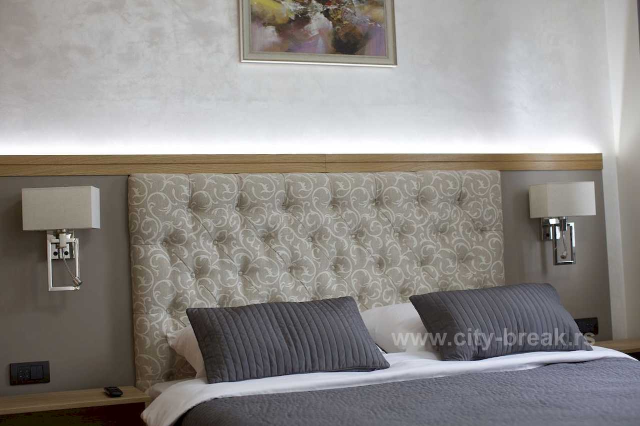 Detalj bračnog kreveta sa tuftovanim uzglavljem, LED trakom iznad kreveta i zidnim lampama – Apartman Merkator – City Break Apartments