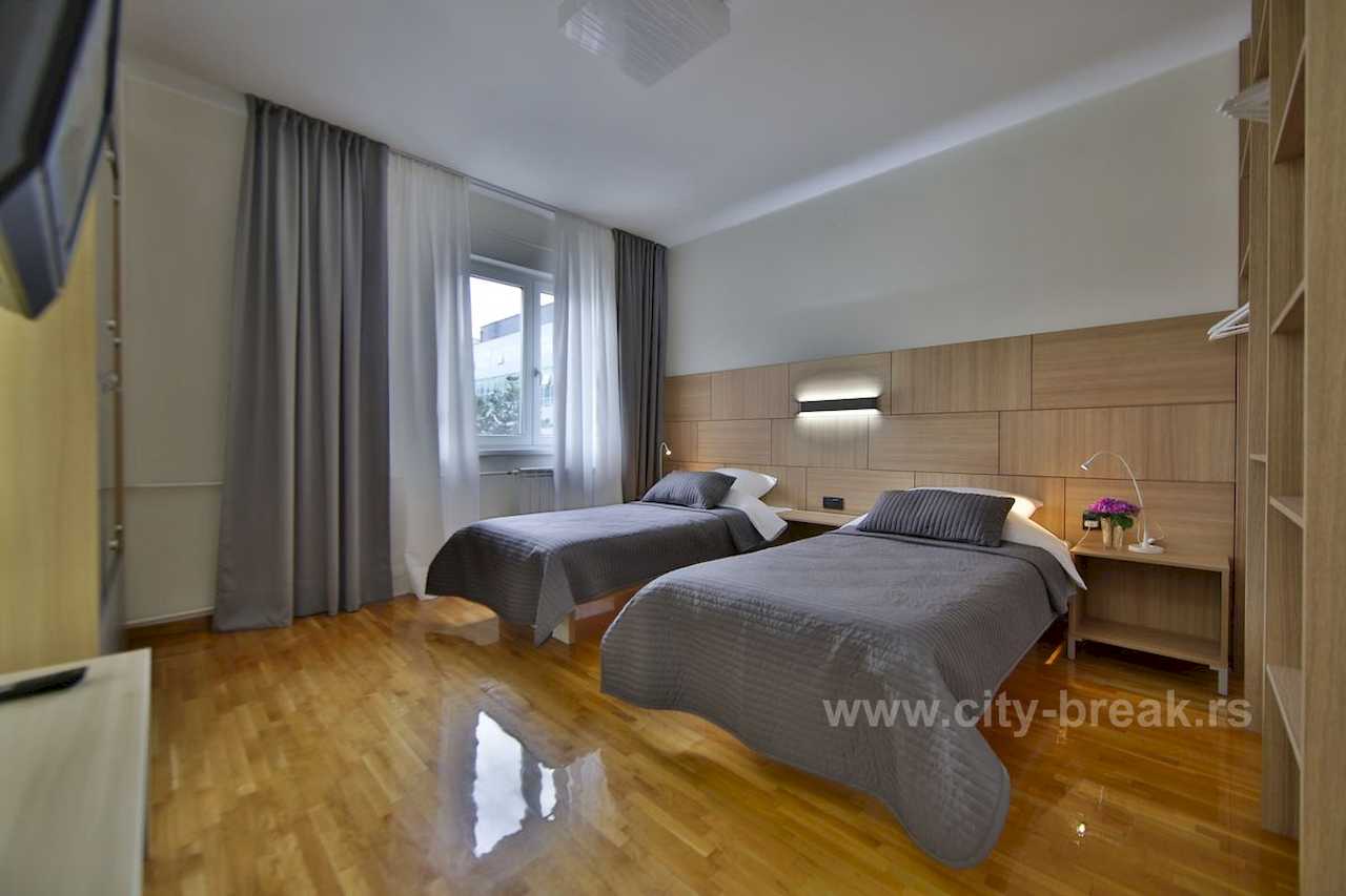 Spavaća soba sa dva singl kreveta, drvenom zidnom oblogom kao uzglavljem – Apartman Merkator – City Break Apartments