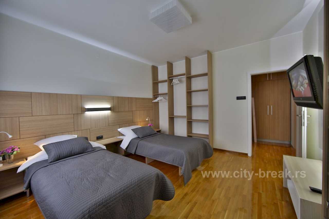 Spavaća soba sa dva singl kreveta, drvenim uzglavljem i otvorenim garderoberom – Apartman Merkator – City Break Apartments