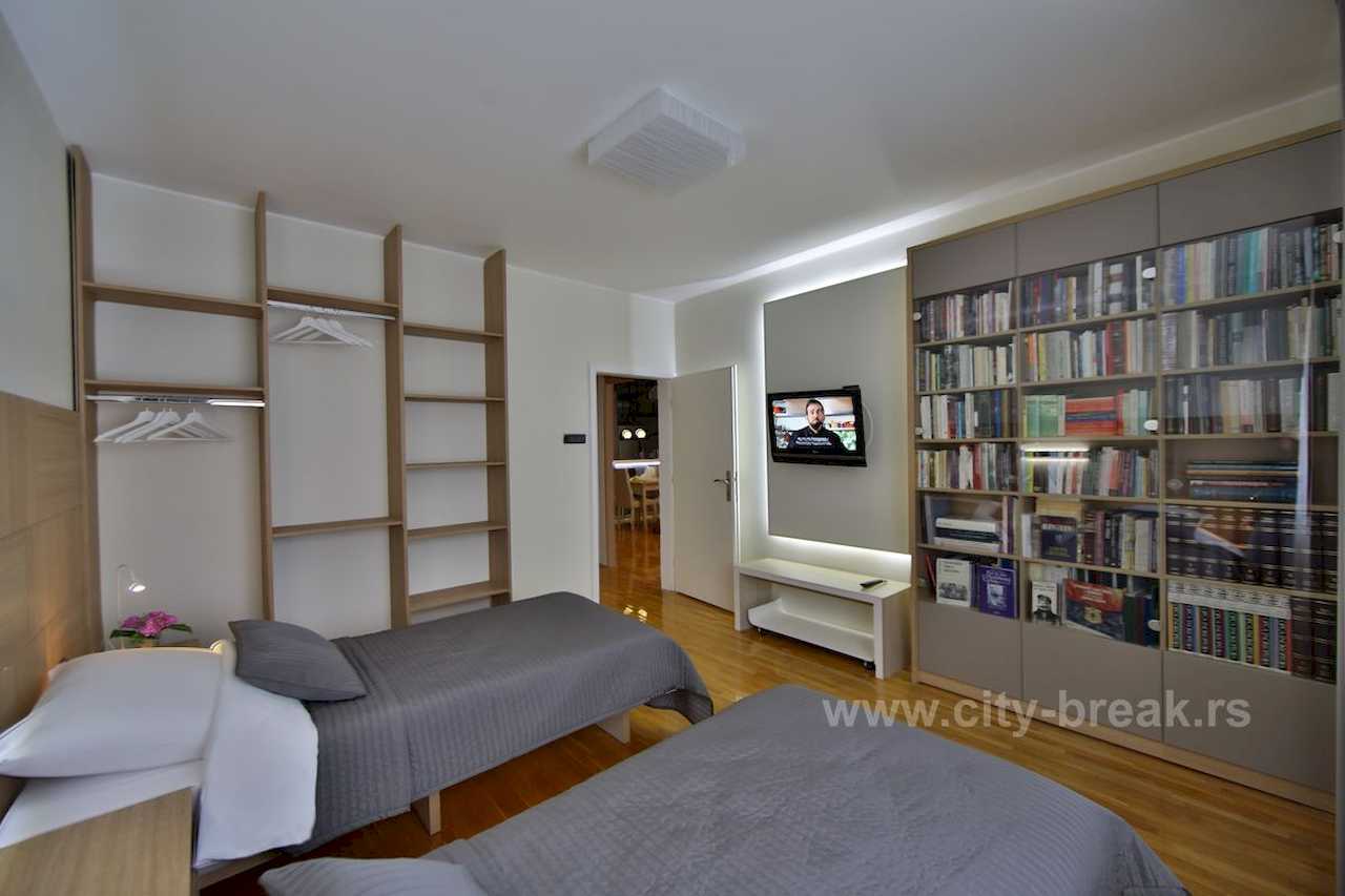 Spavaća soba sa dva singl kreveta, ugradnom bibliotekom sa staklenim vratima i TV-om – Apartman Merkator – City Break Apartments