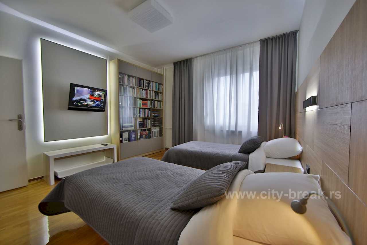 Spavaća soba sa dva singl kreveta, TV-om sa pozadinskim osvetljenjem i policama za knjige – Apartman Merkator – City Break Apartments