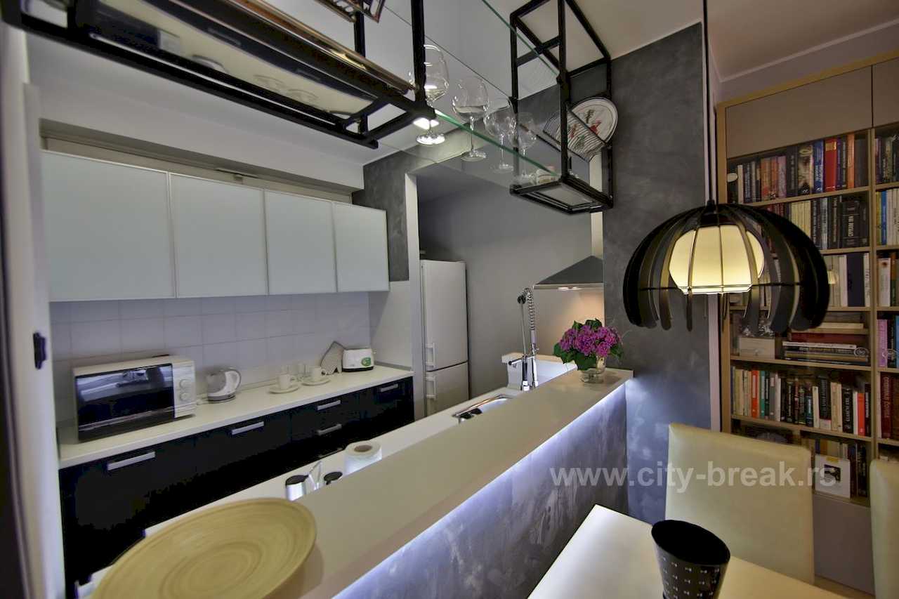 Kuhinja sa crno-belim elementima, LED šankom i velikom bibliotekom u pozadini – Apartman Merkator – City Break Apartments