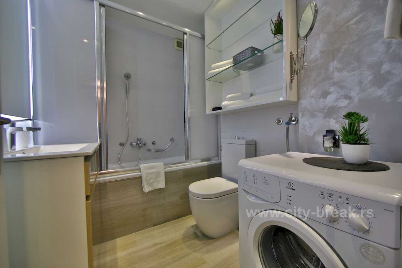 Kupatilo sa kadom i staklenim paravanom, toaletom i veš mašinom – Apartman Merkator – City Break Apartments