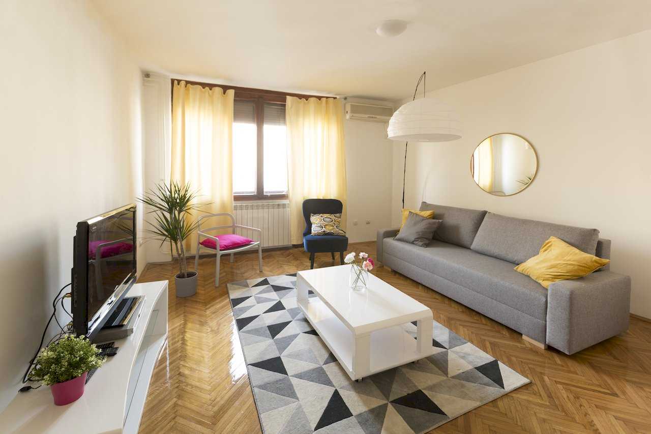 Dnevna soba sa sivom sofom, belim klub stolom, geometrijskim tepihom i TV-om – Apartman Milica – City Break Apartments